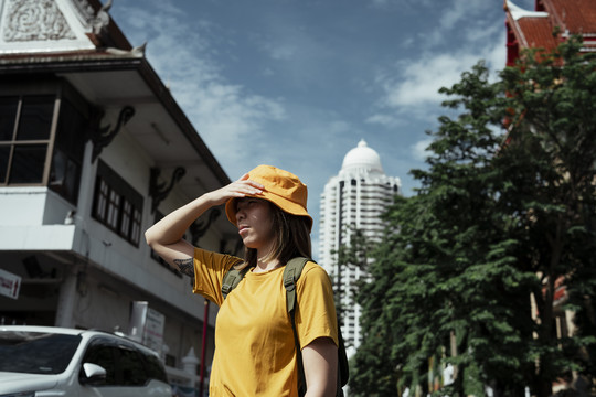 一个穿着黄色t恤的背包女孩在一个城市的寺庙里旅行时抓起帽子。