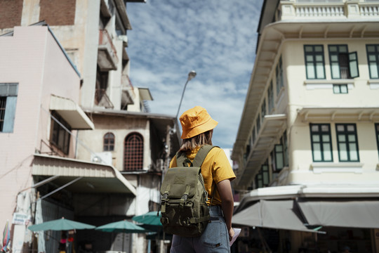 穿着黄色t恤的背包女孩站在当地市场和老城前的后照。