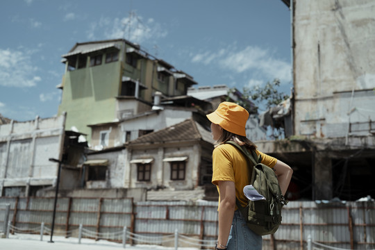 黄色背包女，背着绿色背包，在夏日的阳光下漫步在古老而传统的小镇。