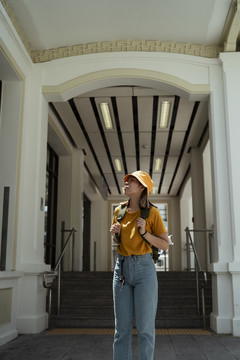 黄色背包女，背着绿色背包，站在白色建筑入口处的灯光下。