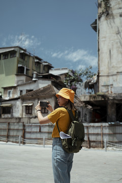 黄色背包女背着绿色背包，在夏日的阳光下，在古老而传统的小镇上拍照留念。