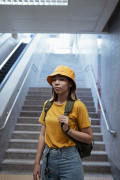 黄色背包女，背着绿色背包，站在地下火车站楼梯的尽头。