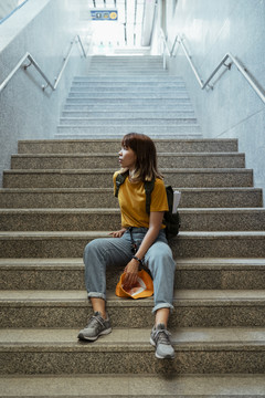 黄色背包女，背着绿色背包，站在地下火车站楼梯的尽头。