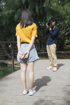 男摄影师拍了一张十几岁的女模特站在公园里的小桥上和坐在桥上的照片。