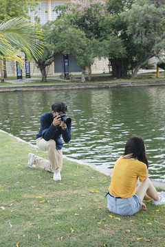 男摄影师坐在公园里的湖边给十几岁的模特拍照。