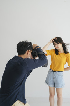 男摄影师在摄影棚里用白色背景拍摄少女模特的照片。