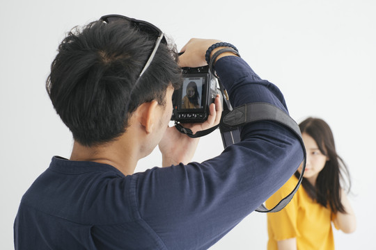 男摄影师在摄影棚里用白色背景拍摄少女模特的照片。