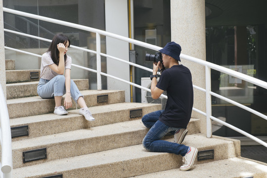 男摄影师坐在鹅卵石楼梯上给模特儿拍照。