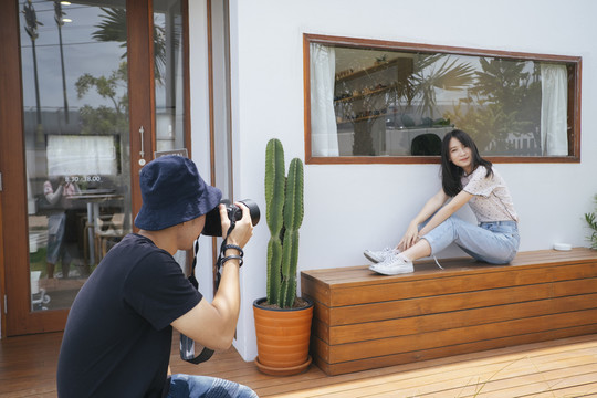 男摄影师在咖啡馆前用仙人掌和木地板给十几岁的模特女孩拍照。