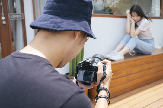 男摄影师在咖啡馆前用仙人掌和木地板给十几岁的模特女孩拍照。