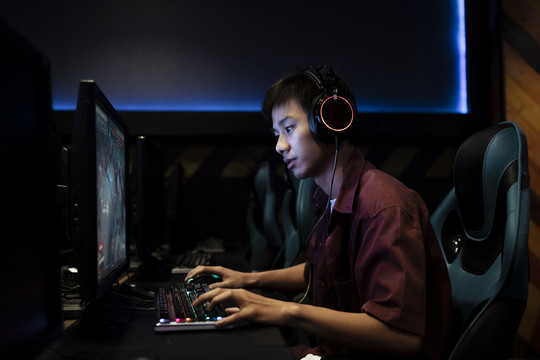 专业玩家戴着耳机在网吧的电脑上玩游戏。在电脑上和队友交谈。