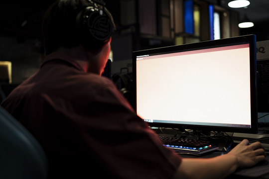 网吧电脑显示器上的白色屏幕空白。年轻的亚洲游戏玩家在红色霓虹灯。