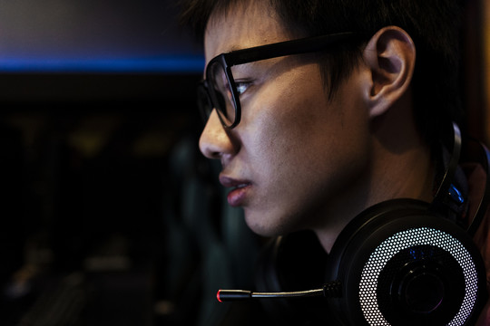 戴着眼镜和耳机的书呆子亚洲青少年游戏玩家的侧视图头像。