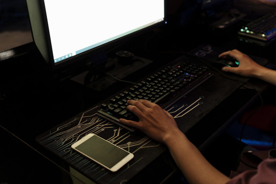 玩家用键盘打字的手。桌子上的黑屏智能手机。显示器上的白色屏幕。