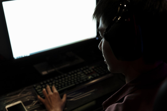 亚洲玩家在电脑上玩电子游戏。白色屏幕显示器。