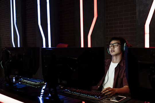 一个亚洲游戏玩家，在玩游戏太久后戴着眼镜，眼睛休息。