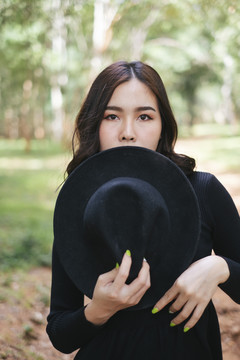 一位穿着黑衣服、戴着黑帽子的女士站在森林里。