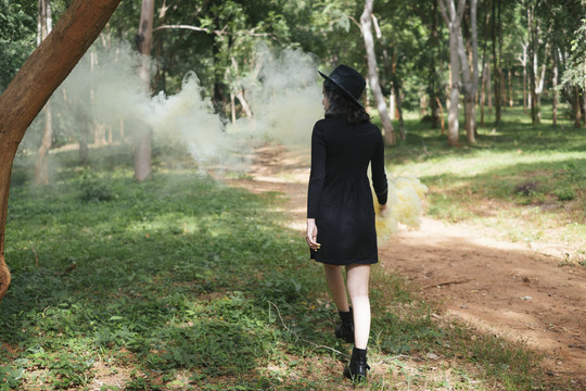 后视图-一个黑衣女巫在森林里玩黄烟手电筒。