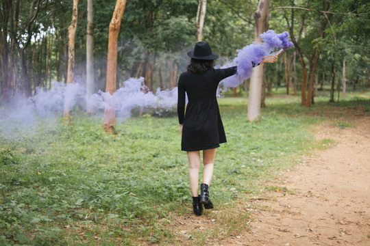 一个黑衣女巫在森林里玩紫烟手电筒。