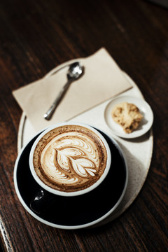 咖啡拿铁艺术在一个豪华的杯子服务与一块饼干在盘子上。