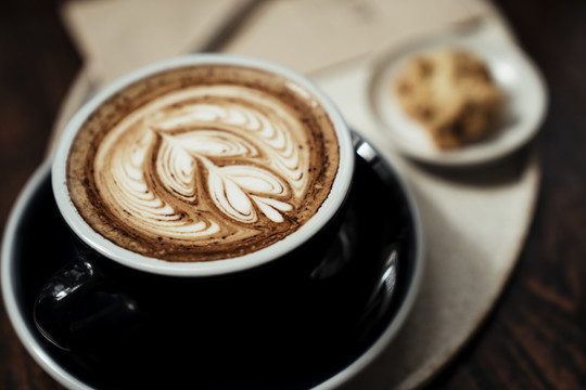 咖啡拿铁艺术在一个豪华的杯子服务与一块饼干在盘子上。