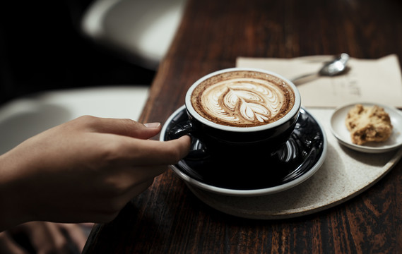 一位顾客拿着一杯咖啡拿铁放在木桌上。