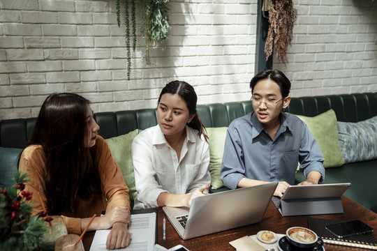 三个年轻的商务人士一起使用笔记本电脑。女商人反对商业策略。年轻的创业者在咖啡馆开会。团队合作理念。