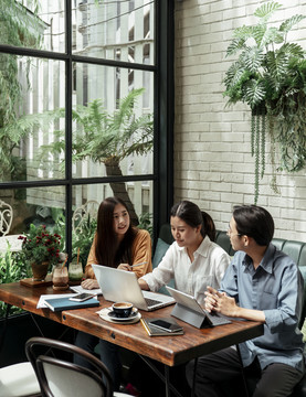 三个年轻的商务人士一起使用笔记本电脑。女商人反对商业策略。年轻的创业者在咖啡馆开会。团队合作理念。