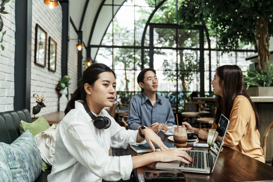 年轻的亚洲女人在美丽的咖啡店里用耳机和笔记本电脑听音乐。