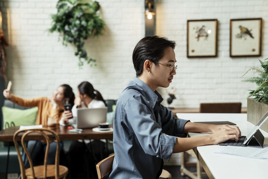 年轻的亚洲商人工作平板电脑，认真地看着城市里的咖啡馆。