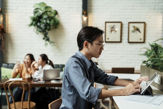年轻的亚洲商人工作平板电脑，认真地看着城市里的咖啡馆。