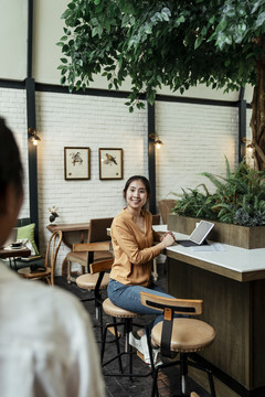 有趣的亚洲年轻女子看到她的朋友出现在咖啡馆里感到惊讶。