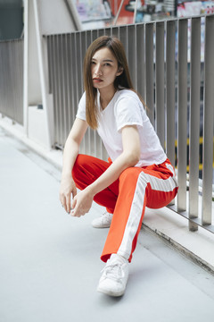 时尚写真-穿着白衬衫和红色运动裤的美丽亚洲年轻女子坐在地板上。