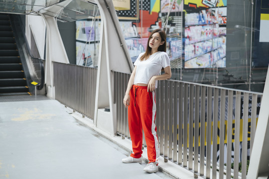 时尚写真-美丽的亚洲年轻女子，穿着白衬衫和红色运动裤，靠在扶手上。