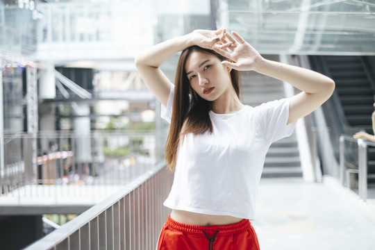 时尚写真-美丽的亚洲年轻女子穿着白衬衫和红色运动裤，性感的姿势双手放在头上。