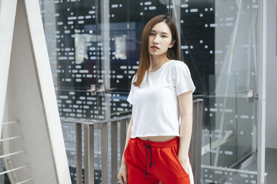 时尚写真-美丽的亚洲年轻女子在白色衬衫和红色运动裤在美丽的现代城市镜子背景。