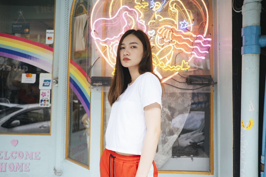 时尚写真-身着白色衬衫和红色运动裤、霓虹灯背景的泰国亚裔年轻女子。