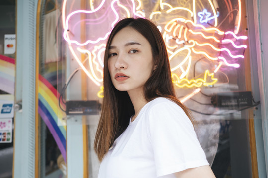 时尚写真-特写年轻的亚泰女性在霓虹灯背景下穿着白色衬衫。