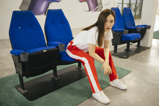 时尚写真-美丽的亚洲年轻女子穿着白衬衫和红色运动裤坐在蓝色的椅子上。
