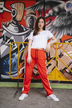 时尚写真-身穿白衬衫和红色运动衫的泰国亚裔年轻女子坐在时髦的涂鸦背景上。