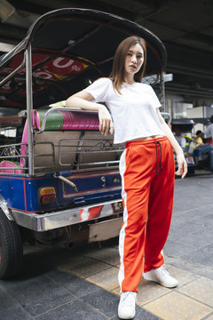 全长时尚肖像-美丽的亚洲年轻女子在白衬衫和红色运动裤站在后面的笃笃笃在人行道上的交通工具。