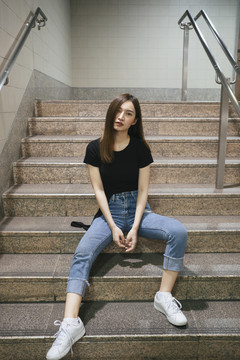 全长时尚写真-美丽的亚洲年轻女子穿着黑色衬衫和牛仔裤长裤坐在地下楼梯。