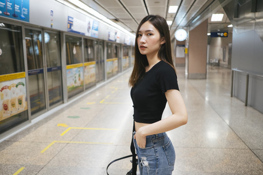 时尚写真——身穿黑色衬衫和牛仔裤长裤的泰国亚裔年轻女子在地铁站台等火车。