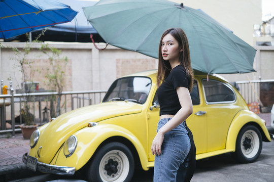 时尚写真-身着黑色衬衫和牛仔裤的泰国亚裔年轻女子，黄色复古汽车背景。