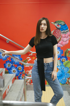 时尚写真-身穿黑色衬衫和牛仔裤裤子的泰国亚裔年轻女子在红色楼梯上涂鸦。