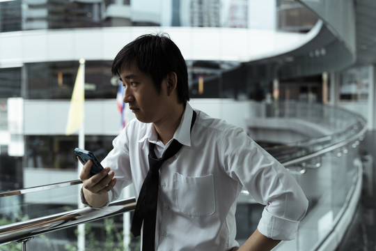 年轻的亚洲混混商人在城市里使用智能手机。