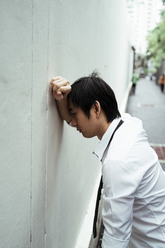 年轻的亚洲商人面朝墙，把手放在墙上。有压力的亚洲商人摆出愤怒的姿势。