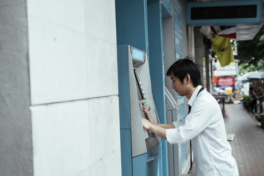 亚裔商人在ATM机上查他还剩多少钱。