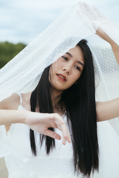年轻的亚洲长发黑发女子新娘在户外戴着白色面纱的肖像。