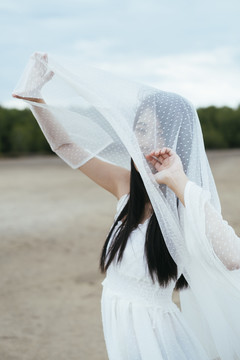 年轻的亚洲长发黑发女子新娘在户外戴着白色面纱的肖像。